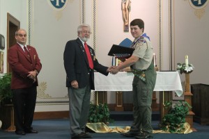 Dennis DeWild presents Austin Perrin with a Flag and Certificate of Recognition from the Benevolent and Protective Order of Elks as Roger McQueen looks on.